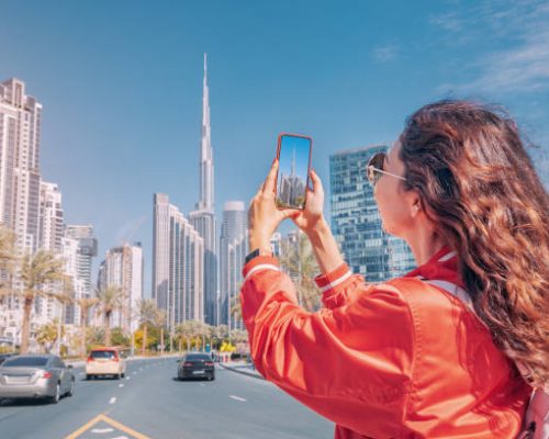 Tourist happy girl taking photos for her travel blog, in Dubai downtown district against background of the Burj Khalifa highest skyscraper